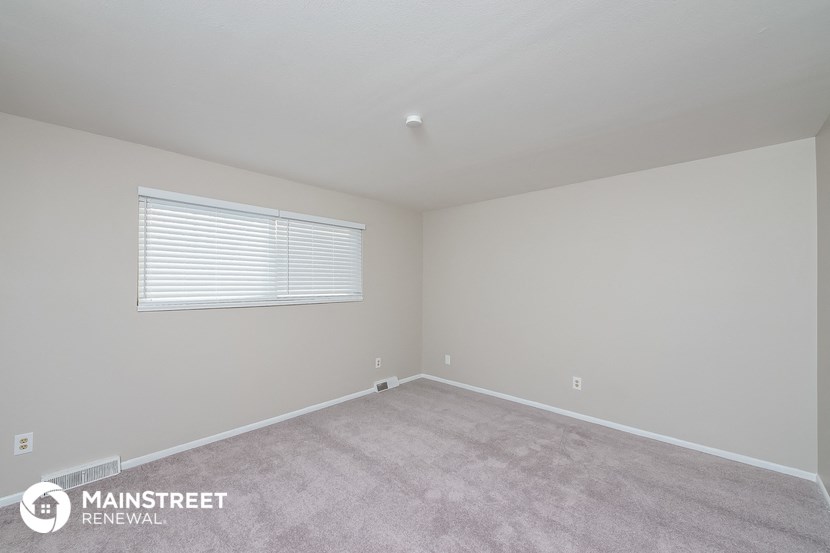 the spacious bedroom with carpeted flooring and a window
