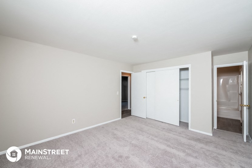 a master bedroom with white walls and carpet and a door to a closet