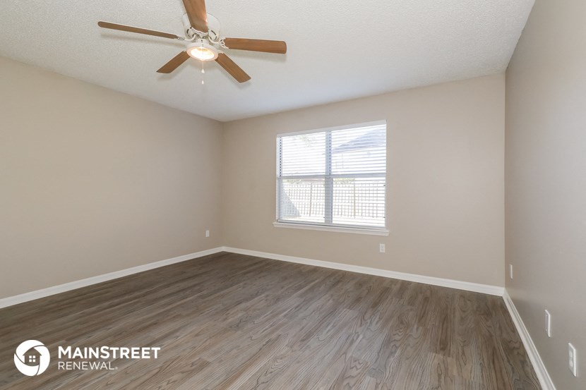 the spacious living room with wood flooring and a ceiling fan