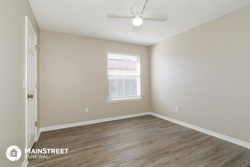 the spacious living room of an apartment with wood flooring and a ceiling fan