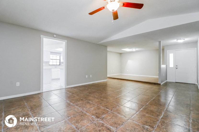 an empty living room with tile flooring and a ceiling fan