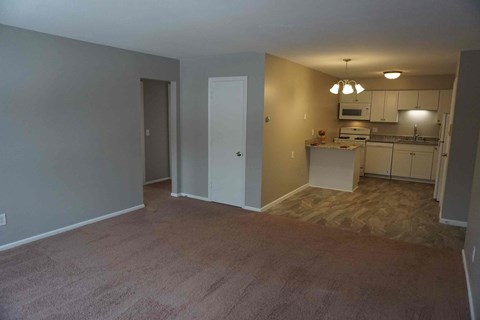 an empty living room with a kitchen in the background