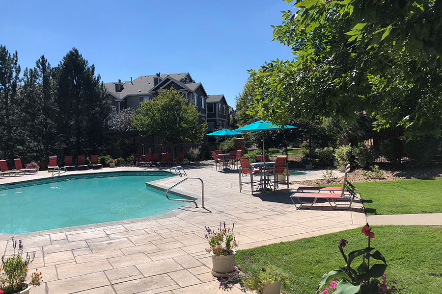 Westlake Greens Pool Deck with turquoise umbrellas, orange chairs, and green grass