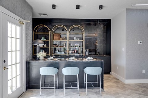 A kitchen with a bar area featuring a black counter and three white bar stools.