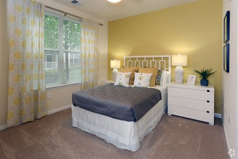 A bedroom with a bed, nightstand, and window with curtains.