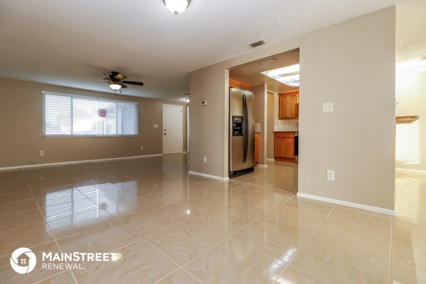 an empty living room and kitchen with tile flooring and a ceiling fan