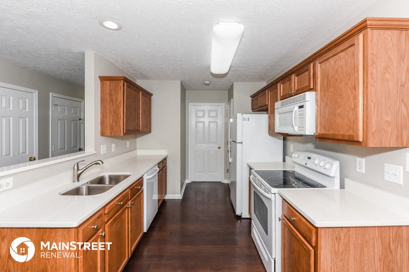 a kitchen with wood cabinets and white counters and appliances and a door to a hallway