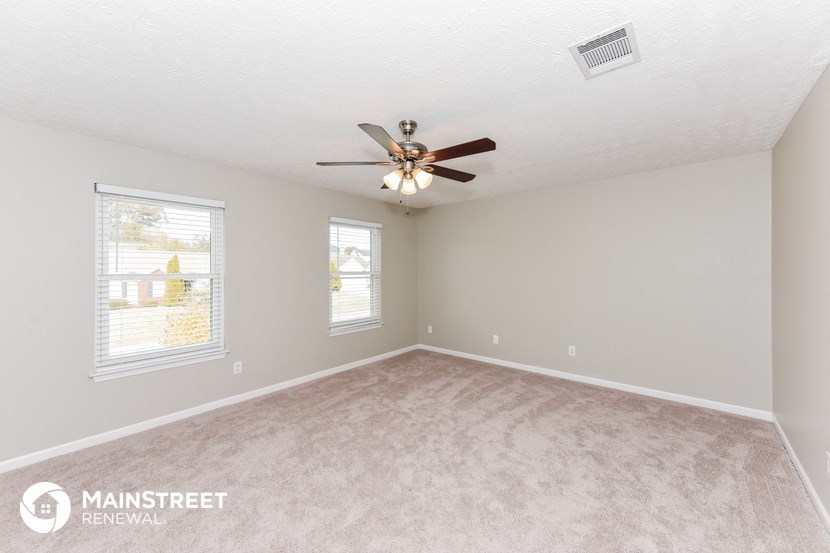 the spacious living room with ceiling fan and carpeting