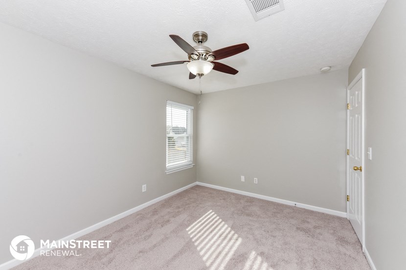 the spacious living room of this manufactured home has a ceiling fan and carpeting