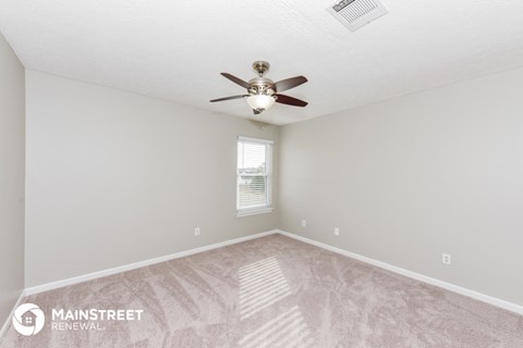 the spacious living room with ceiling fan and carpet