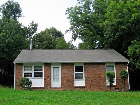 A small house with a white door and windows surrounded by greenery.
