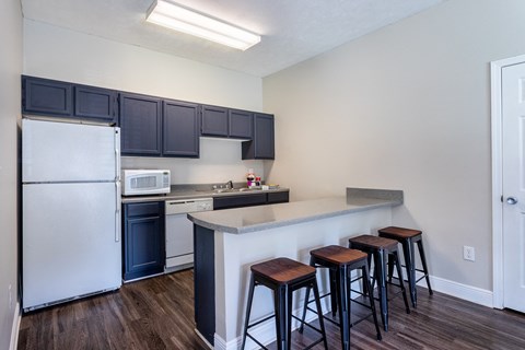 A kitchen with a white refrigerator, black cabinets, and a white countertop with three bar stools.