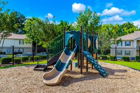 A playground with a slide and a green fence.