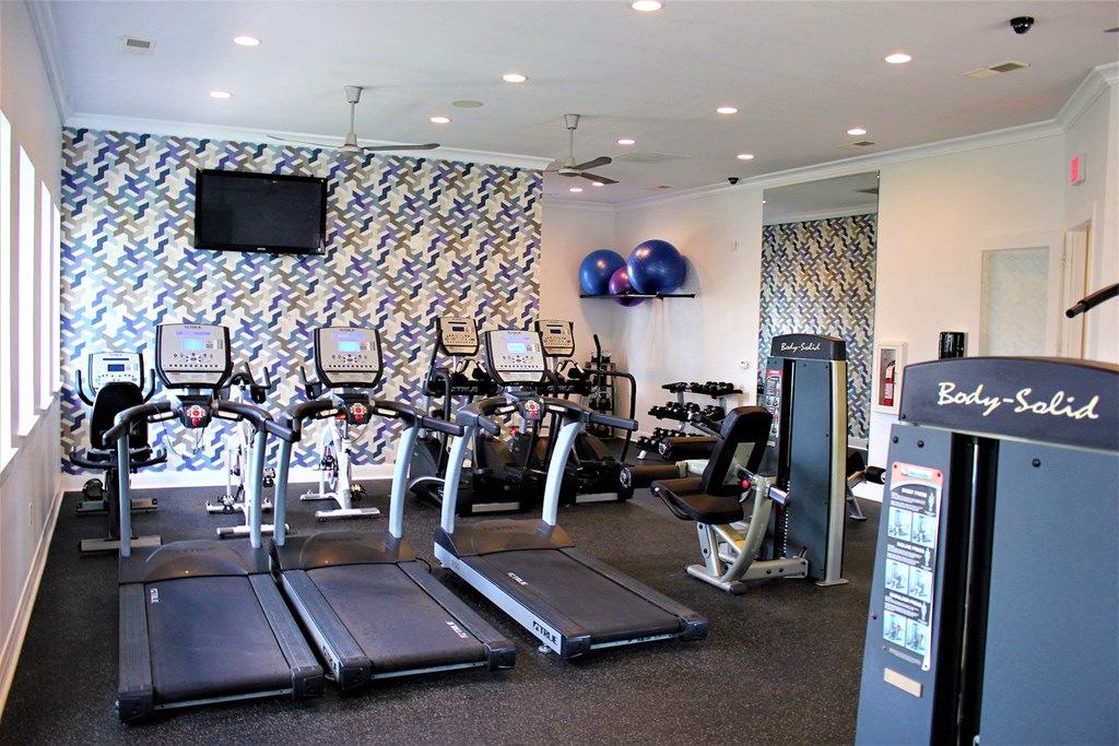 a gym with cardio equipment and a tv on the wall