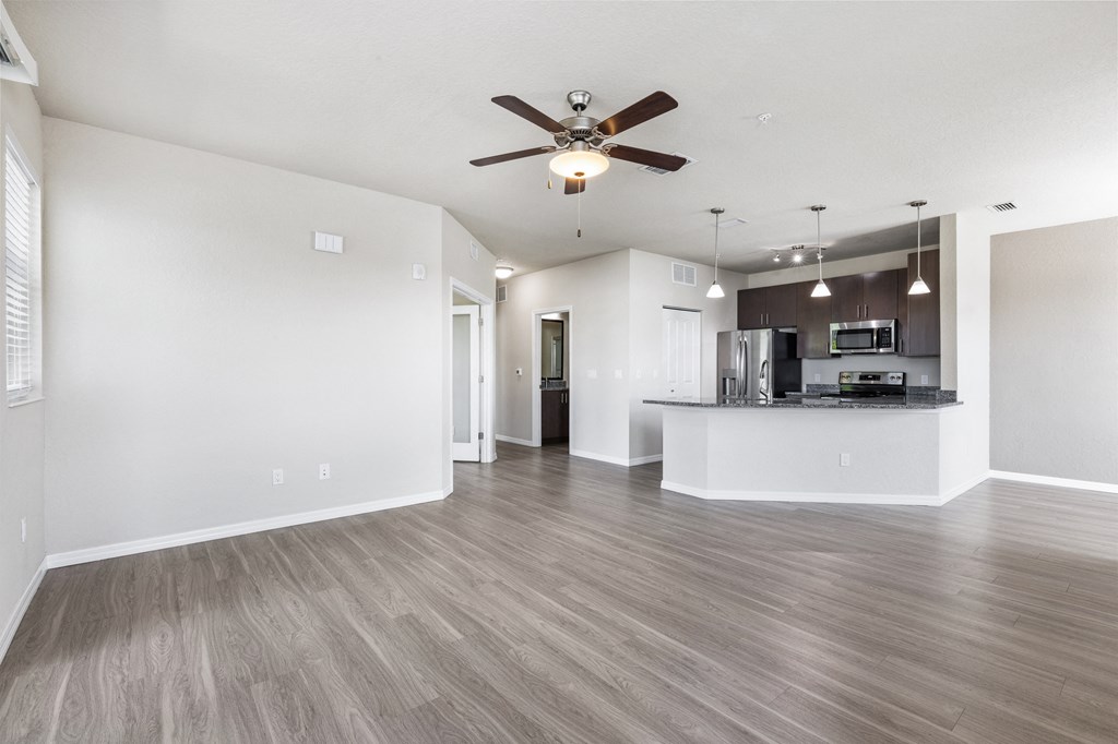 an empty living room with a ceiling fan and a kitchen