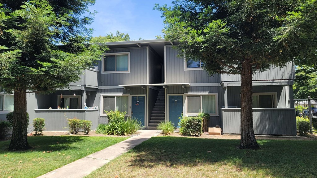 the exterior of an apartment building with a sidewalk and trees