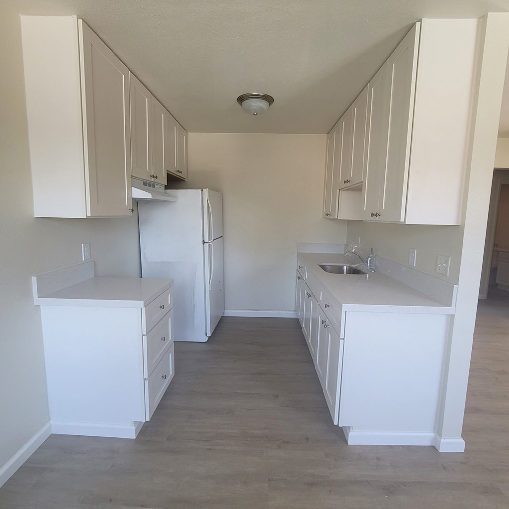 an empty kitchen with white cabinets and a refrigerator