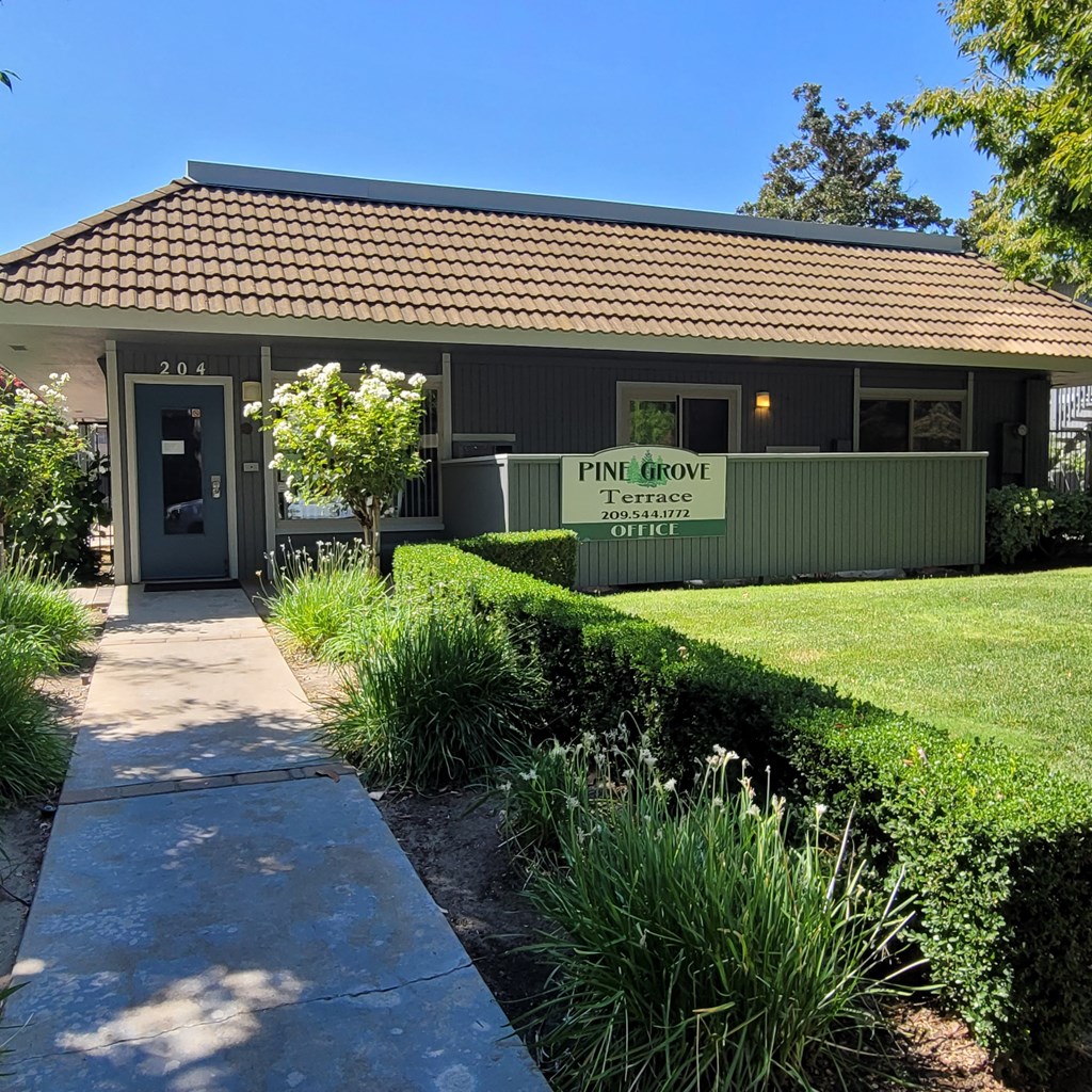 the front of a green building with a sidewalk and grass