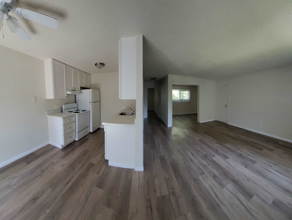 an empty living room and kitchen with wooden floors and white cabinets