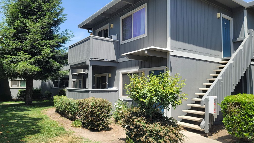 the front of a grey house with a yard and stairs