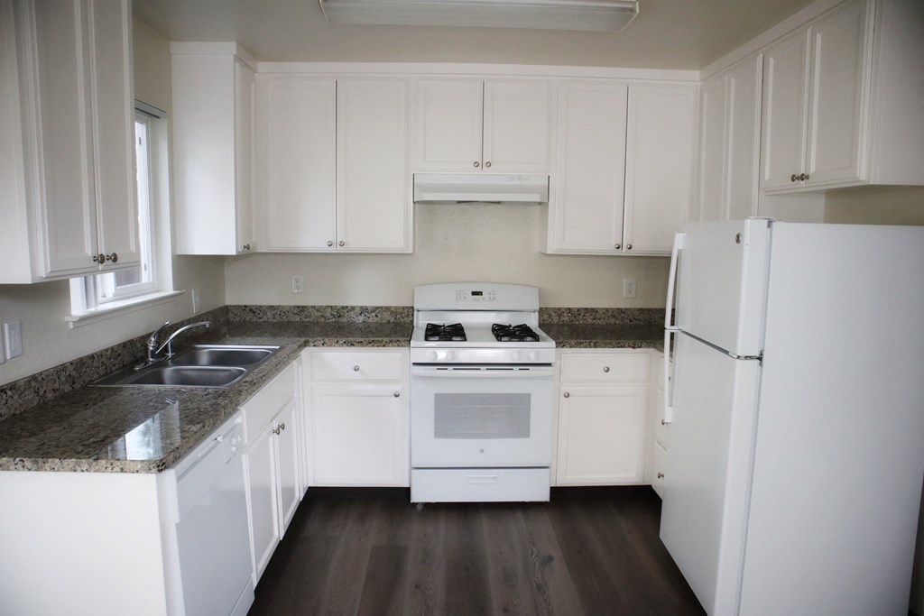 A white kitchen with a stove top oven and a refrigerator.