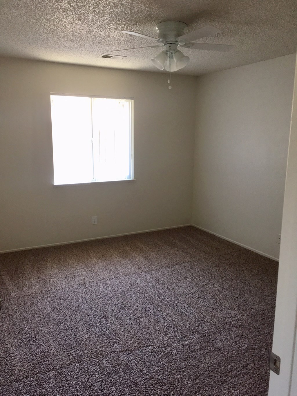 A room with a ceiling fan and a window letting in sunlight.