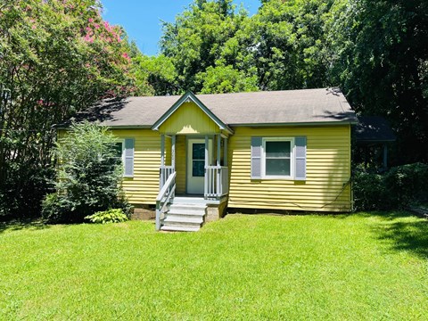 A yellow house with a porch and a green lawn.