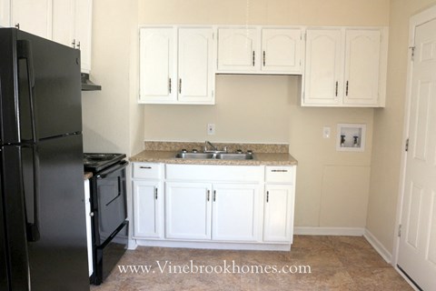 A black refrigerator is in the corner of a kitchen with white cabinets.