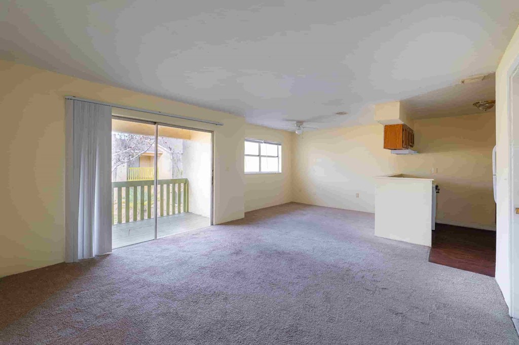 an empty living room with a sliding glass door to a balcony