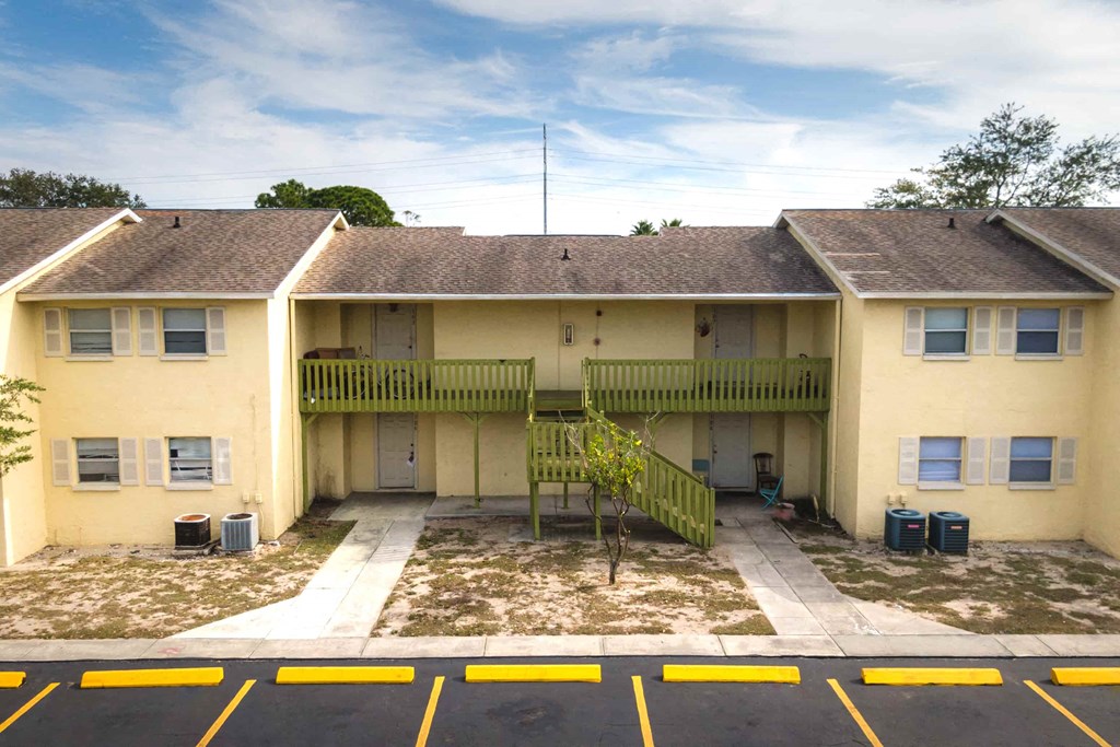 an apartment building with yellow walls and a yard with trash cans