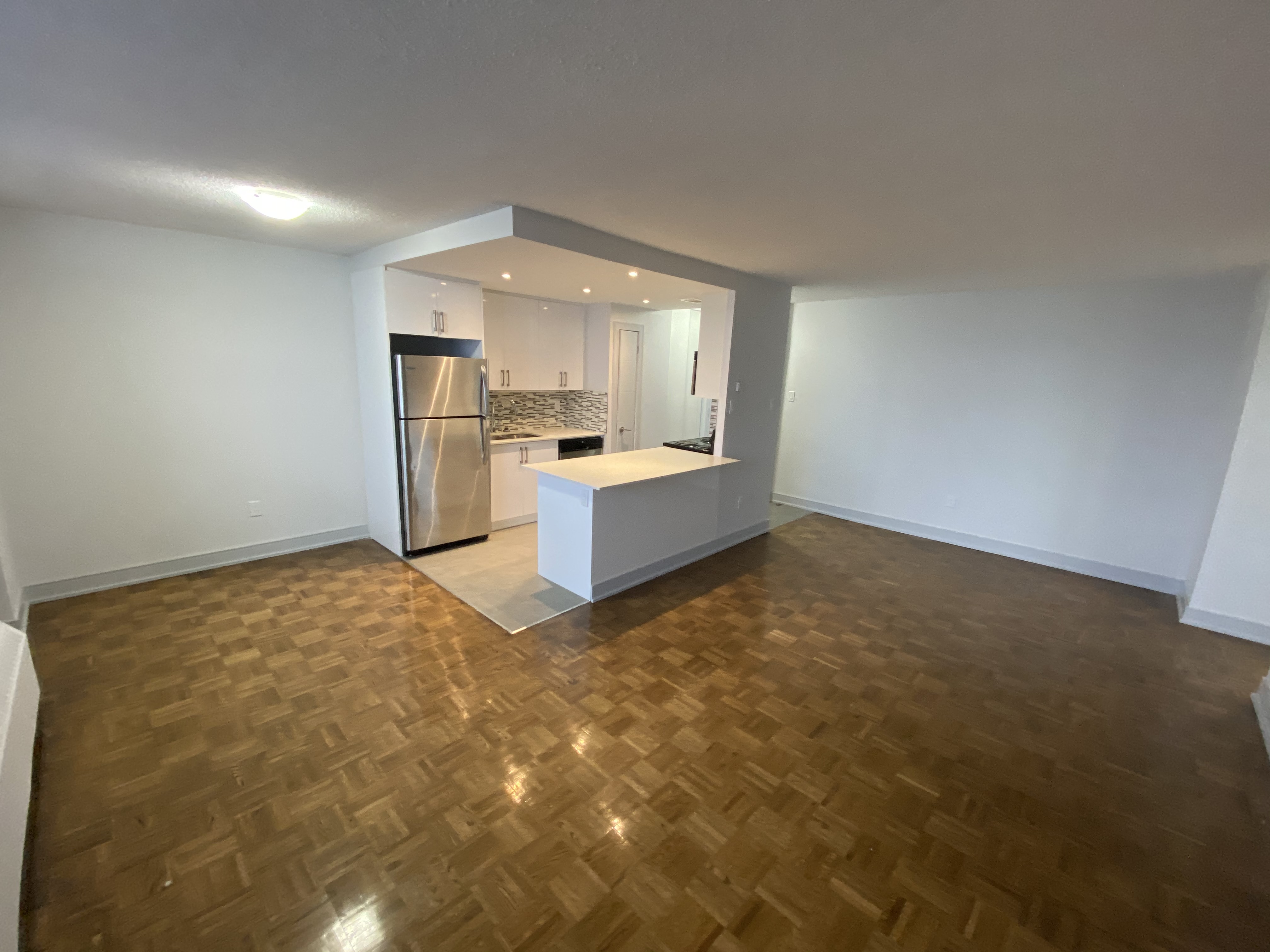 an empty living room with a kitchen and wood flooring