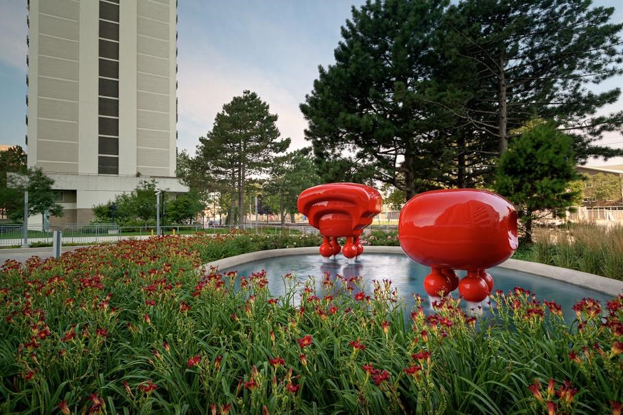 two red heart sculptures in the grass near a fountain