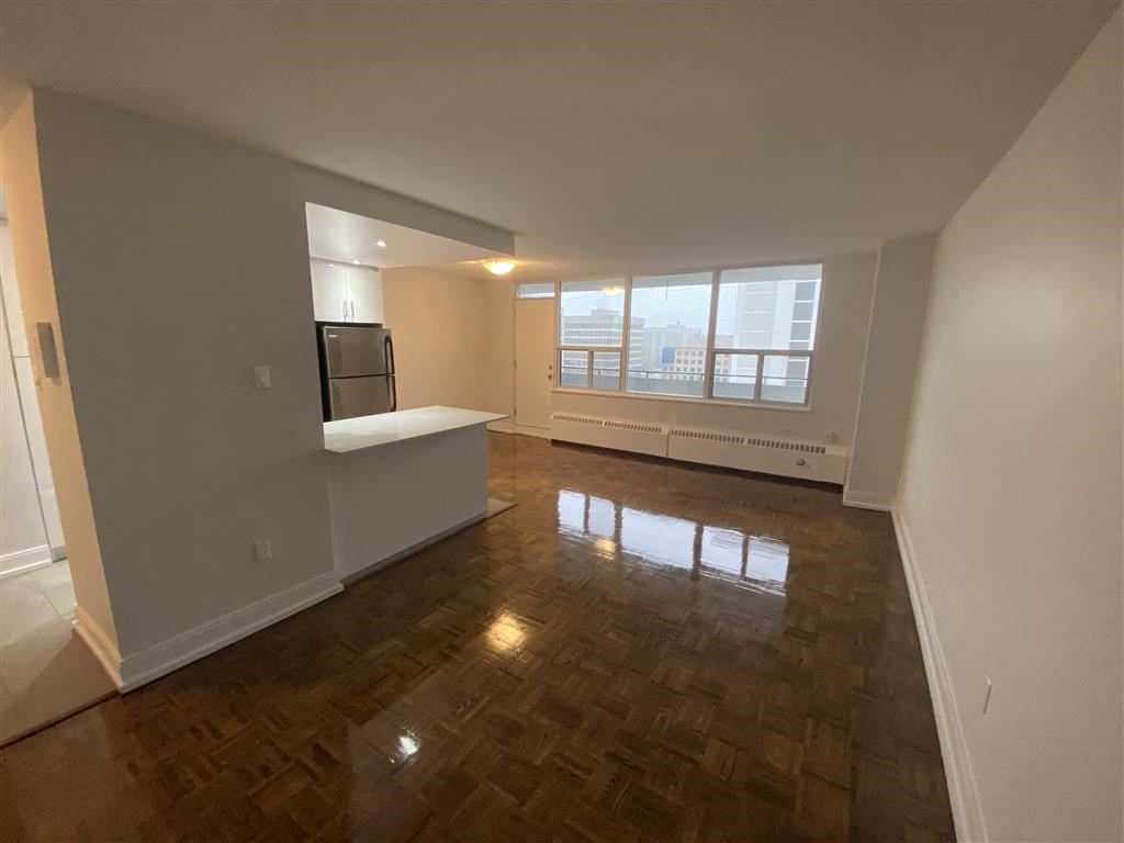 an empty living room with a kitchen and a large window
