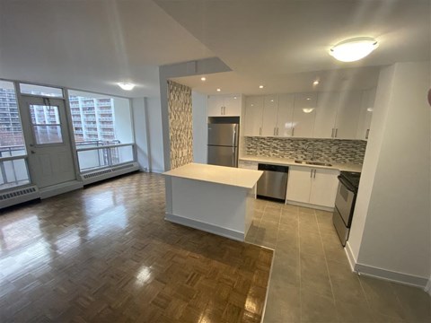 an empty living room with a kitchen and a window