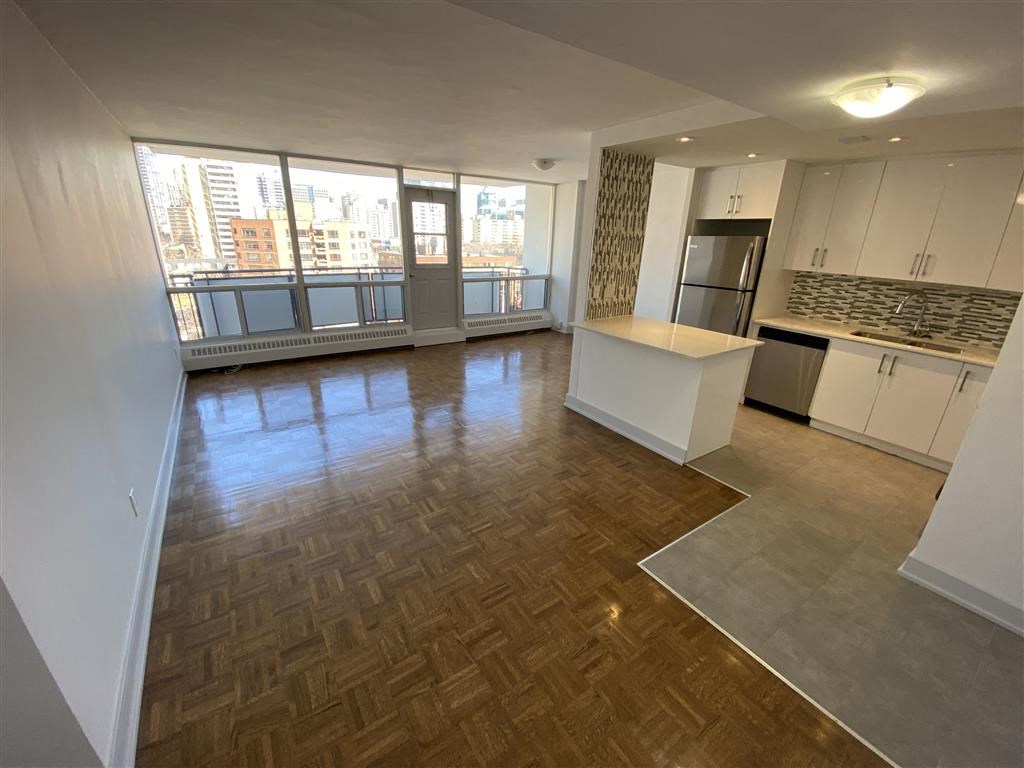 an empty living room with a kitchen and a large window