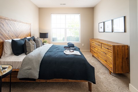 A bedroom with a bed, nightstand, and a window with blinds.