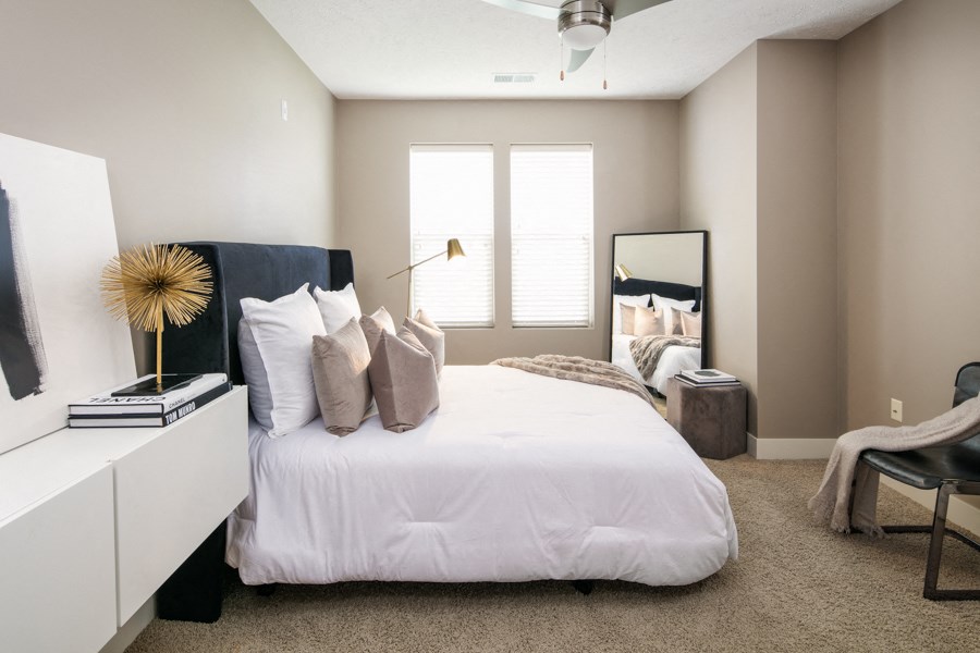 A bedroom with a large bed, a ceiling fan, and a window with blinds.