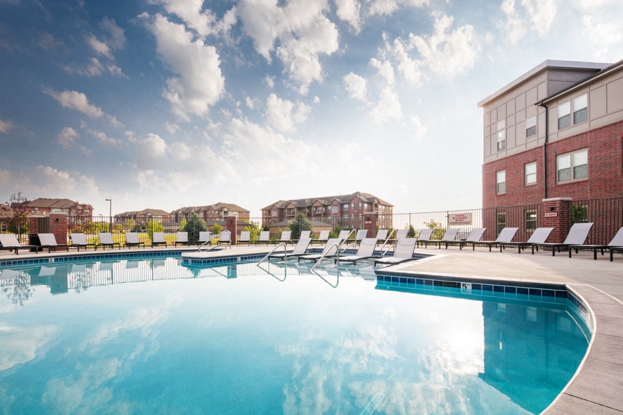 A large swimming pool with sun loungers and a building in the background.