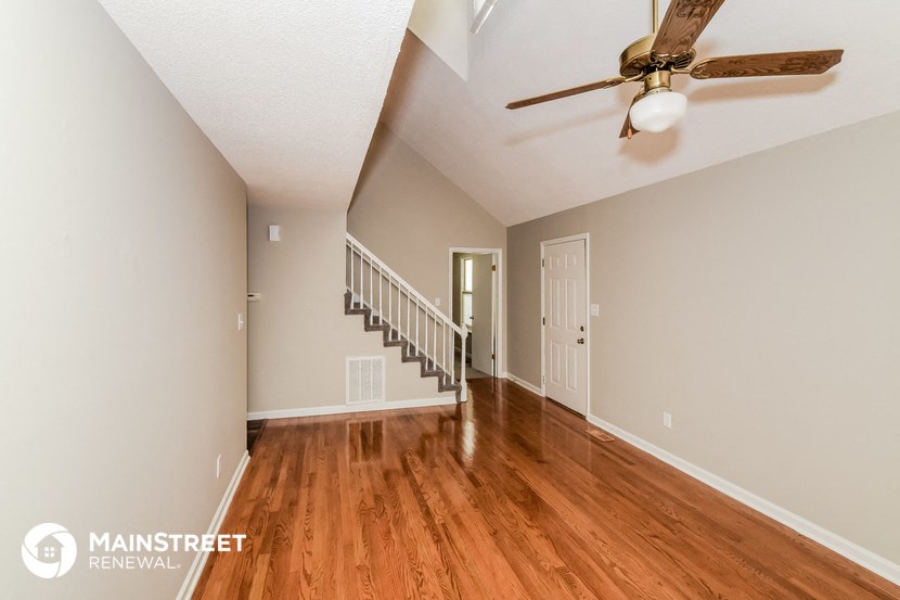 the living room and entryway of a house with wooden floors and a ceiling fan
