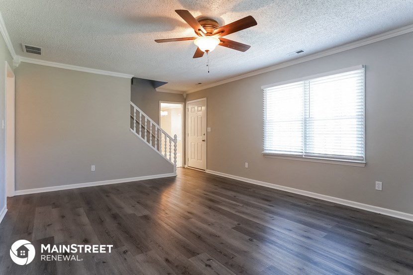 the spacious living room with hardwood flooring and a ceiling fan