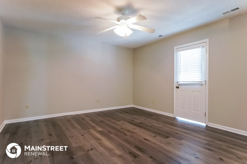 the spacious living room of an empty home with wood flooring and a ceiling fan