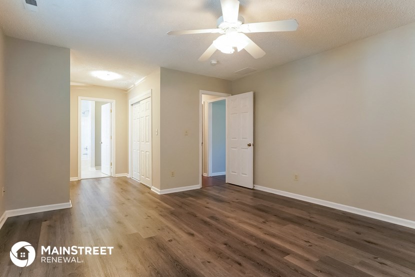 the living room and dining room of an apartment with wood floors and a ceiling fan