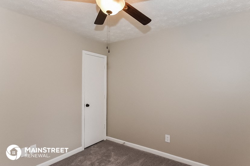 the bedroom of an apartment with a ceiling fan and a door