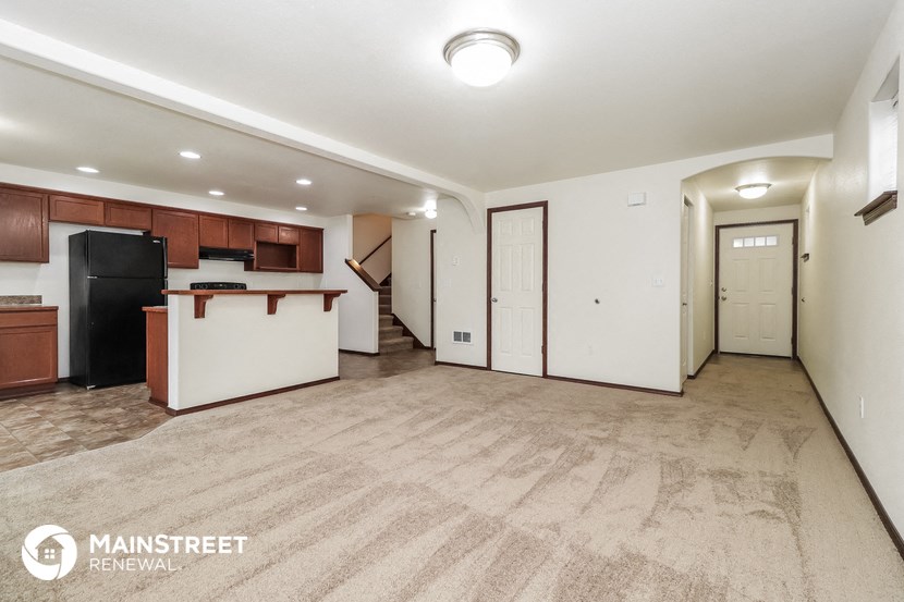 the living room and kitchen of an apartment with white walls and wood cabinets