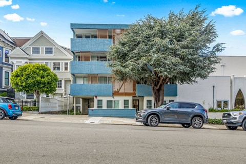 A grey car is parked in front of a blue building.