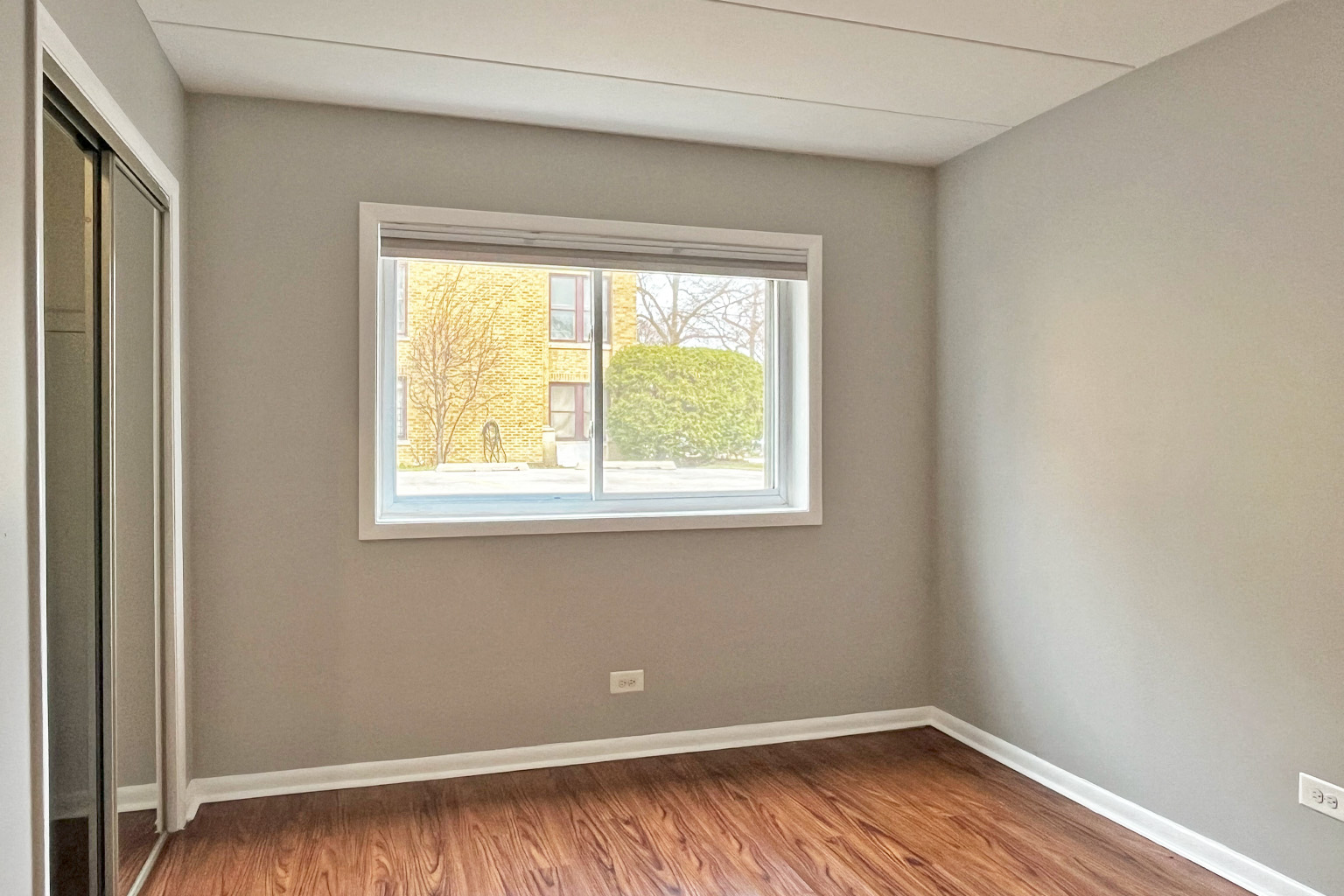 A room with a window showing a view of a building and trees outside.