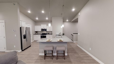 a kitchen with a large island with two chairs and a stainless steel refrigerator