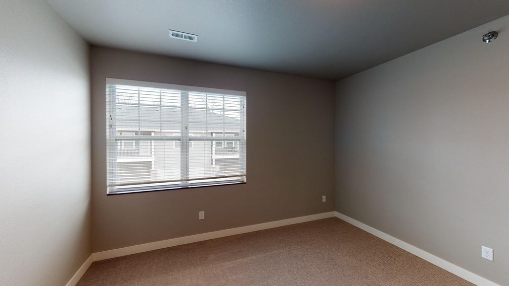 an empty bedroom with a large window and brown carpet