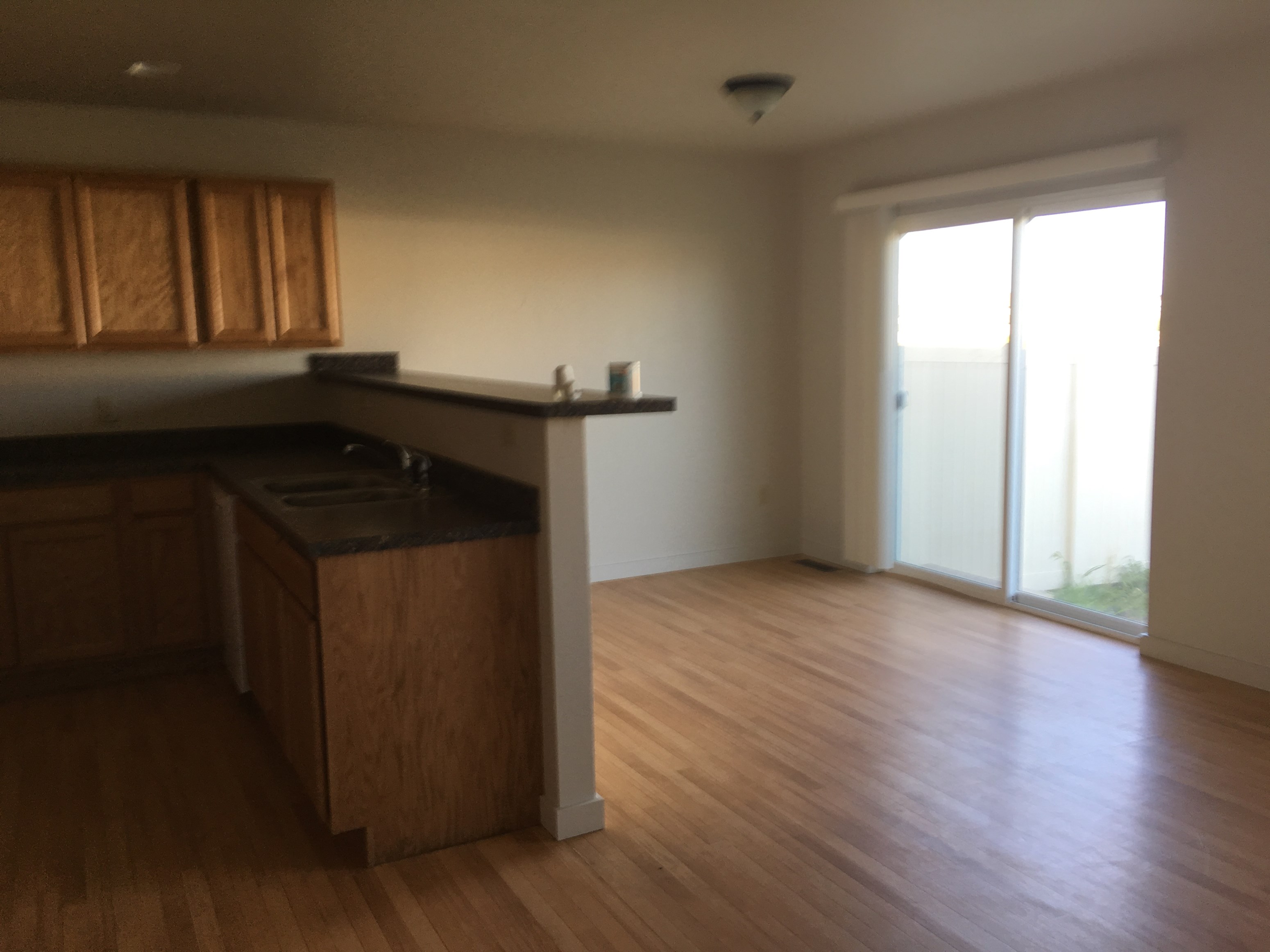 an empty kitchen and living room with wood flooring and a sliding glass door