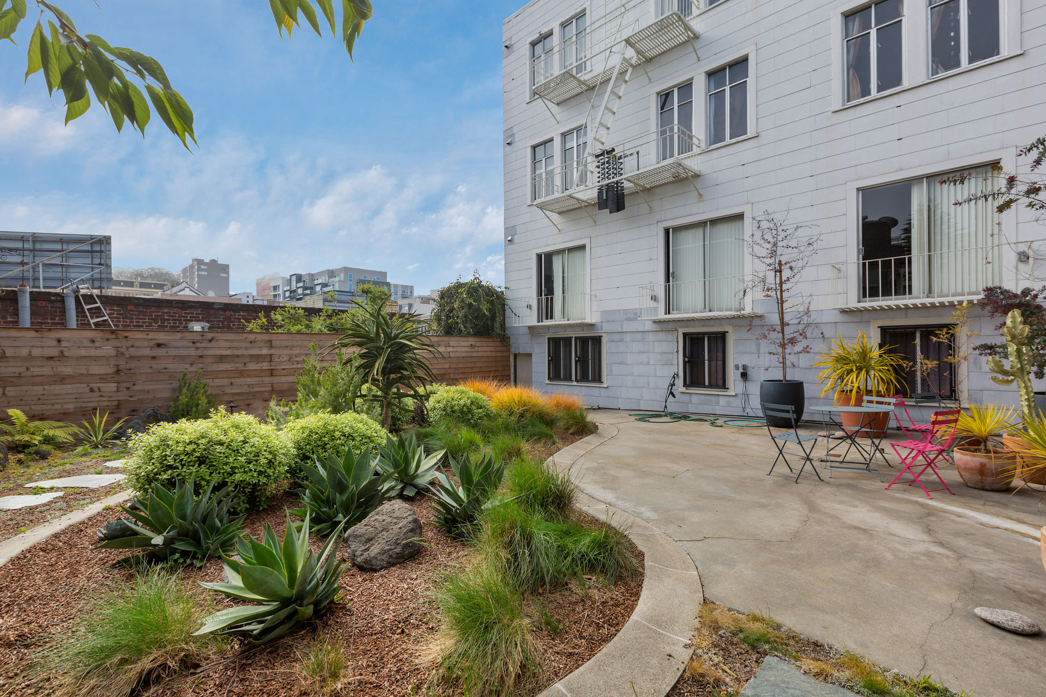 A white building with a balcony and a patio with chairs and plants.